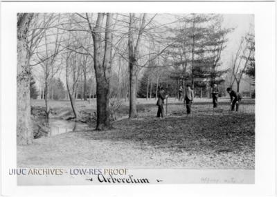 Black and white photograph showing 5 men with surveying equipment in a natural landscape with trees. A creek is at the left of the frame.